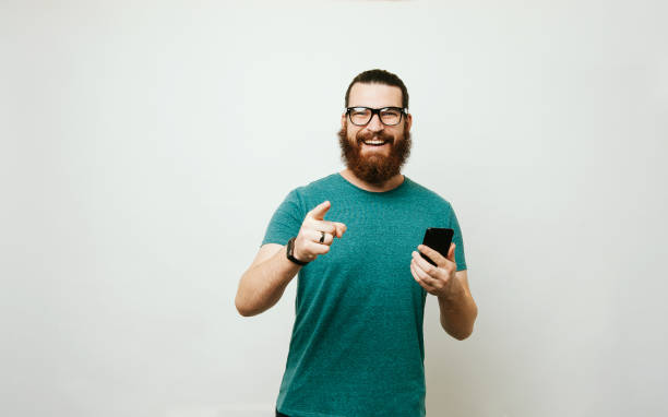 istock Happy bearded hipster man holding smart phone and pointing at the camera 1195123423