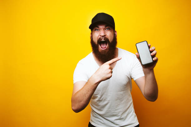 istock Amazed screaming young bearded man pointing at smartphone 1195123465