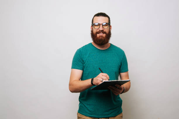 Young bearded man wearing glasses looking at the camera and holding a clipboard. stock photo