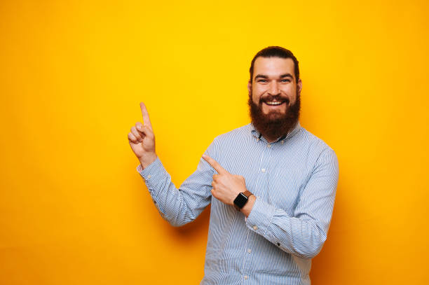 istock Happy cheerful young bearded man smiling and pointing at copyspace over yellow background 1195124333