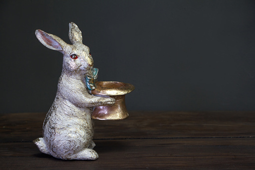 Close up of a white-golden statuette of an Easter bunny holding a empty hat, Easter background or concept, selective focus
