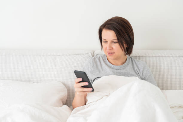 istock Woman using smartphone as she sits in bed covered with duvet 1195134546