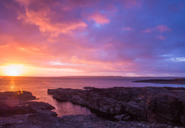 A breathtaking sunset over a rocky coasting and flat ocean horizon. Vibrant colors, interesting foreground, and plenty of copy space.
