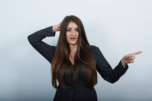 istock Woman over gray wall keeping hand on head, looking at camera, pointing aside 1195158197