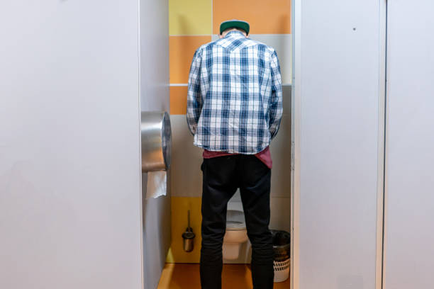 jeune homme dans les toilettes publiques, debout à côté de l'urinoir dans le centre commercial - urinal public restroom male toilet in a row photos et images de collection