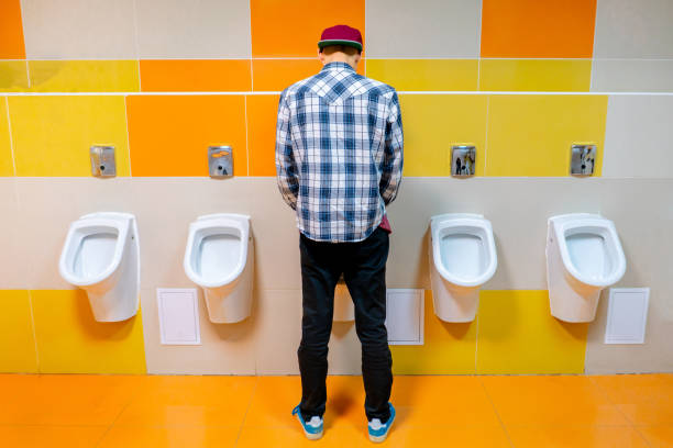 young man in the public toilet, standing next to the urinal in the trade center - urinal clean contemporary in a row imagens e fotografias de stock