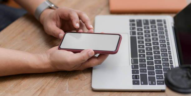 istock Cropped shot of young man using blank screen smartphone while working on his project with laptop 1195174266