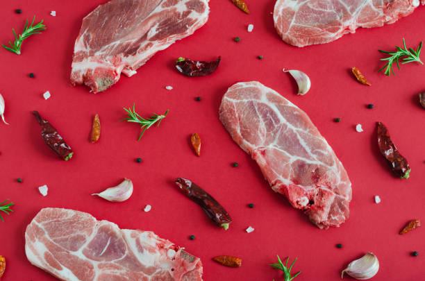 Raw pork steaks with spices on red background. Flat lay.