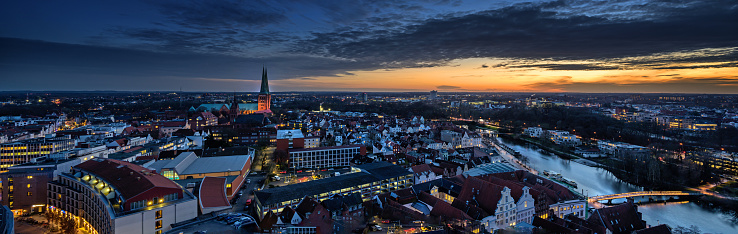 Luebeck, Germany – December 17, 2019:  Aerial night view panorama of the illuminated city of Luebeck in winter with the Cathedral Dom and the river Trave, long term exposure at the blue hour with sunset on a cloudy sky, copy space