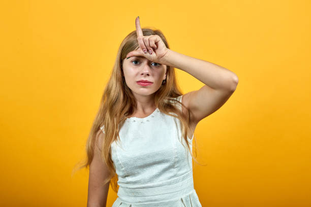 istock Disappointed young lady keeping finger on forehead, doing L loser gesture 1195186919