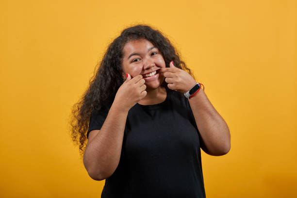 istock Young woman with overweight pulls smile with fingers, looking at camera 1195187840