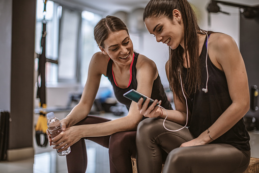 Two attractive sportswomen in the gym sitting down and reading text messages