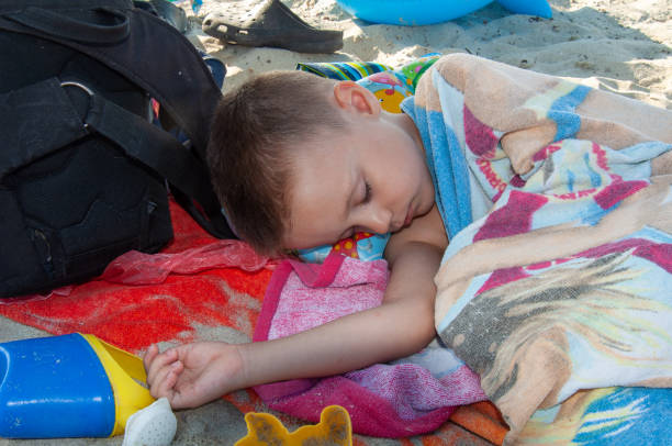 Cute blond toddler boy, sleeping on a big round beach chair on the deck of pool next to the beach on tropical island of Mauritius