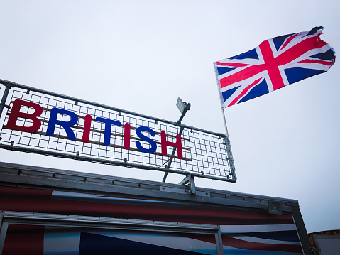 Sign for British in patriotic colors standing next to UK Union Jack flag flying in bleak gray sky