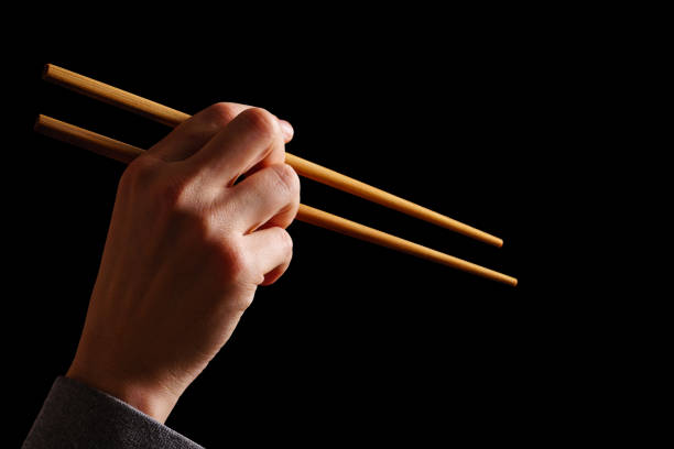 main femelle avec des baguettes en bois. main retenant les bâtons traditionnels de bambou de sushi pour la nourriture chinoise, japonaise, thaïlandaise ou asiatique, d'isolement sur le fond noir avec l'espace de copie. - traditional culture flash photos et images de collection