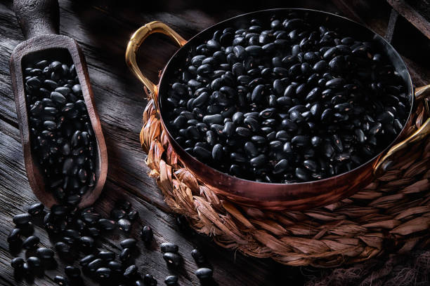 Close-up low key image of black beans in cooper cooking pot on rustic wooden table