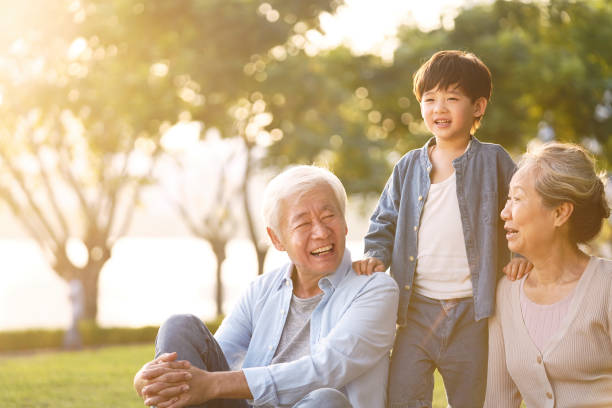 asian grandparent and grandson having fun outdoors in park asian grandson, grandfather and grandmother sitting chatting on grass outdoors in park at dusk china chinese ethnicity smiling grandparent stock pictures, royalty-free photos & images