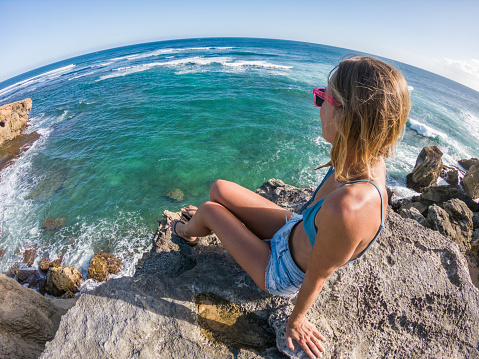 Young woman sitting on rocks by the sea contemplating view