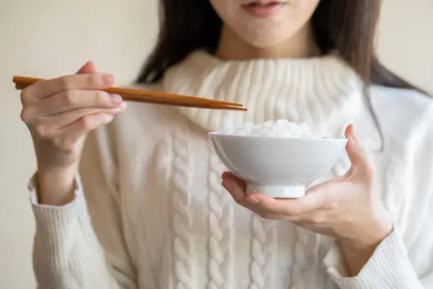 Woman holding white rice and chopsticks in a bowl