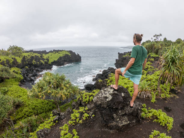 istock Young man on rocks by the sea contemplating view 1195238170