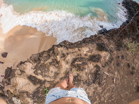 Personal perspective of woman sitting on cliff above beach