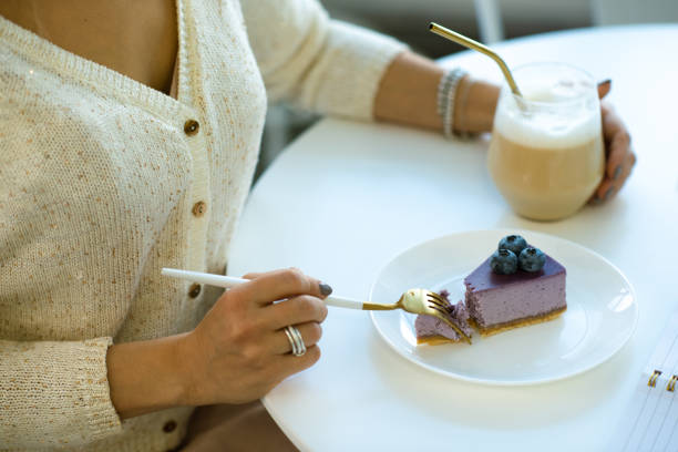 Hands of young woman having cappuccino and eating blueberry cheesecake
