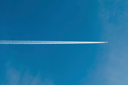 A plane flying through blue skies with condensation trails from the wings
