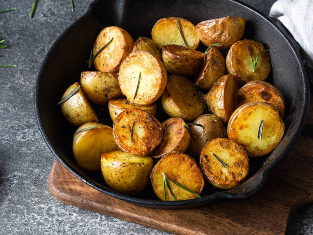 istock Black cast iron pan with fried roasted potato wedges with herbs on dark gray background 1195246510