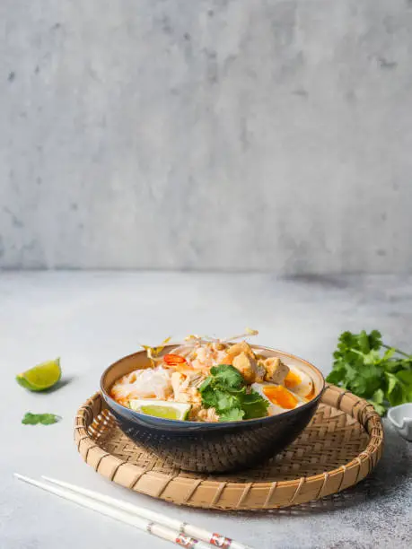 Malaysian noodles laksa soup with chicken, prawn and tofu in a bowl on grey background. Copy space