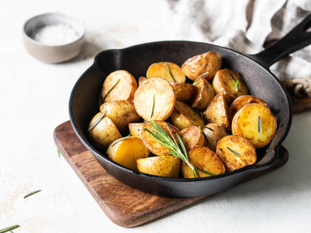istock Black cast iron pan with fried roasted potato wedges with herbs on a light background 1195246571