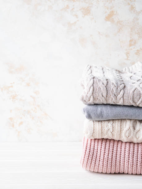 istock Stack of warm knitted woolen sweaters pastel shades against beige textured wall. Copy space 1195246619