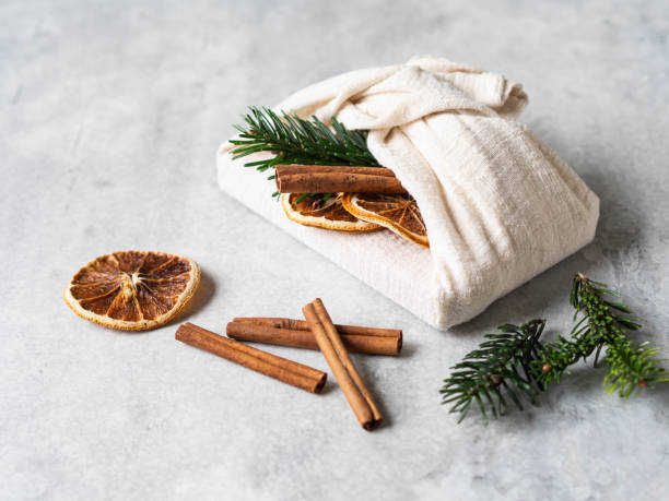 Eco-friendly fabric reusable gift packaging with fir brunch, cinnamon stick and dry orange slice. Christmas reusable sustainable gift wrapping alternative.