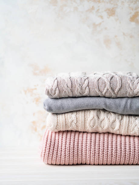 istock Stack of warm knitted woolen sweaters pastel shades against beige textured wall. Copy space 1195246662