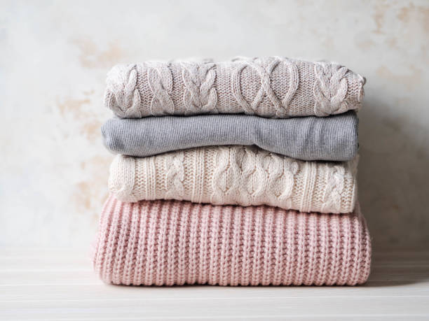 istock Stack of warm knitted woolen sweaters pastel shades against beige textured wall. Copy space 1195246741