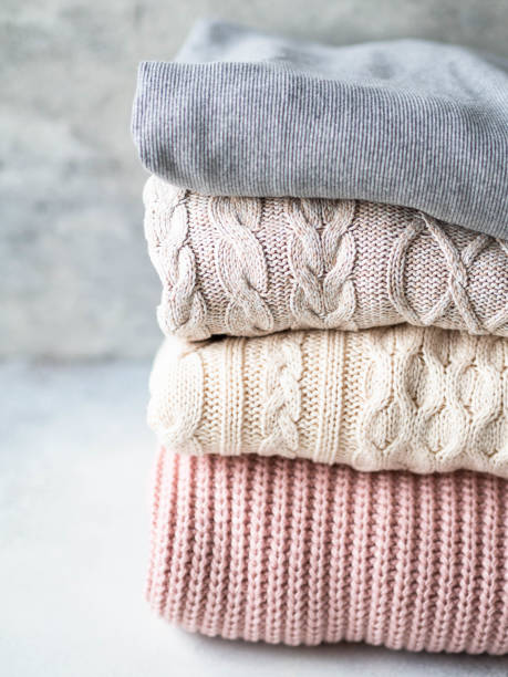 istock Stack of warm knitted woolen sweaters pastel shades against grey wall. 1195246768
