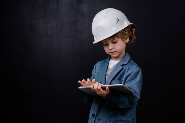 Serious cute little boy in hardhat and formalwear using digital tablet