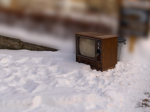 Antique television set thrown on a snowy sidewalk