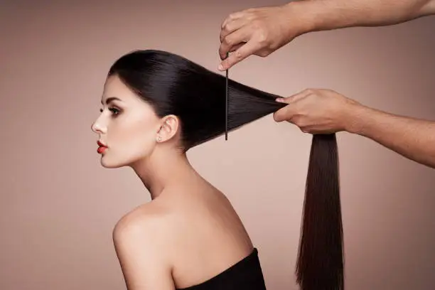 Hairdresser combs the hair of a woman. Portrait of beautiful young woman getting haircut. Care for long smooth hair