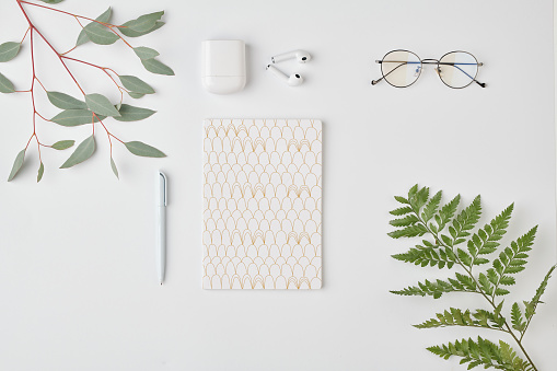 Flatlay of notebook with pen, eyeglasses and earphones on white background
