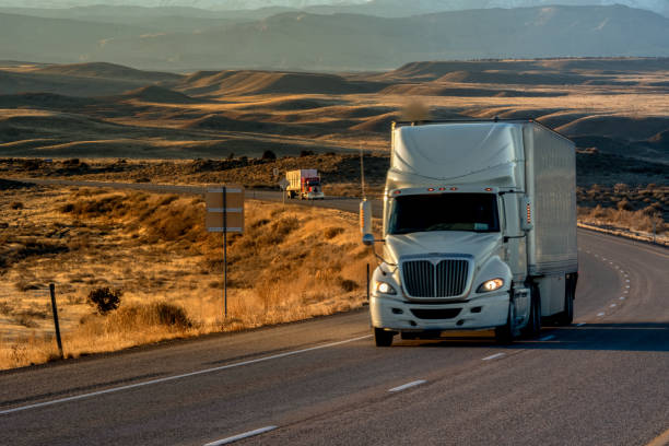 long haul semi-truck rolling down a four-lane highway at dusk - four lane highway stock-fotos und bilder