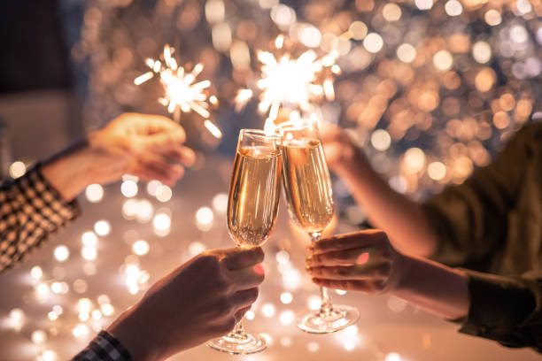 manos de pareja con flautas de champán y sus amigos con luces de bengala - año nuevo fotografías e imágenes de stock