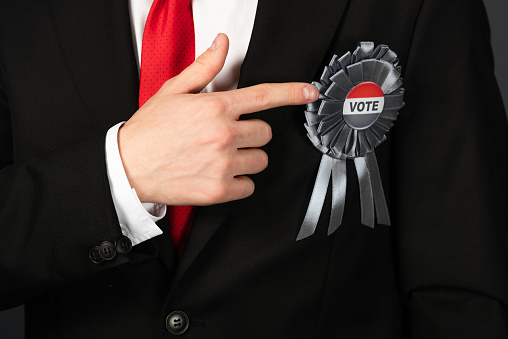cropped view of man in black suit pointing with finger at badge with vote lettering