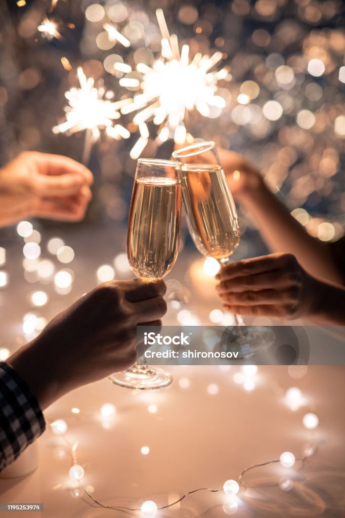 Manos de amigos sosteniendo flautas de champán y brillantes luces de bengala - Foto de stock de Año nuevo libre de derechos