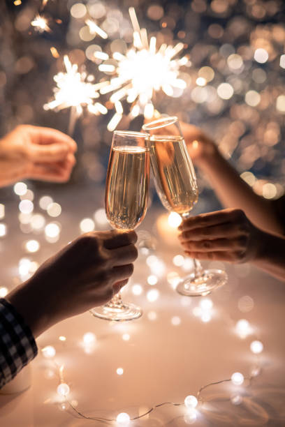 manos de amigos sosteniendo flautas de champán y brillantes luces de bengala - new year fotografías e imágenes de stock
