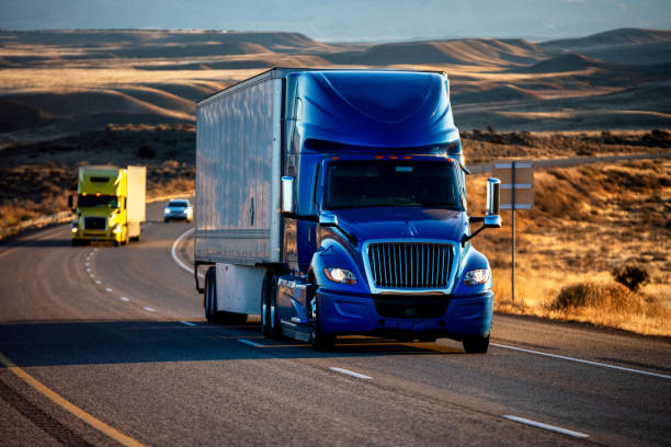 long haul semi-truck rolling down a four-lane highway at dusk - véhicule utilitaire et commercial photos et images de collection