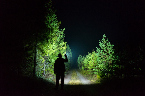 Man standing outdoor at dark night shining with flashlight. Mystical and abstract photo of Swedish nature and landscape.