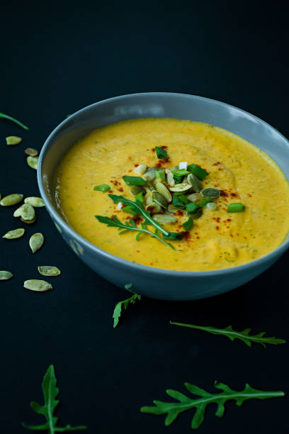 Pumpkin soup with cream and pumpkin seeds, served in a light bowl, top view. Proper and healthy food. Black background.