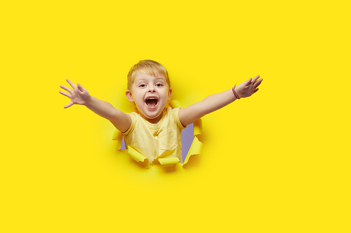 Little surprised child looking, peeping through the bright yellow paper hole. Advertise childrens goods. Happy childhood concept. Copy space for text.