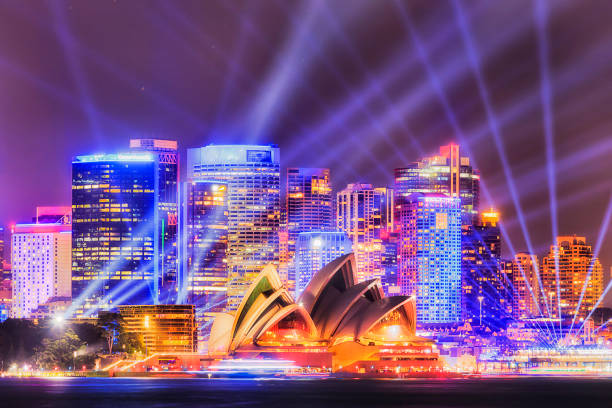 Sy VIvid 19 Crem 180mm rays Wall of high-rise office towers on Sydney city waterfront of Circular quay during annual light show with bright blue beams in dark sky over major city landmarks across the harbour. sydney stock pictures, royalty-free photos & images