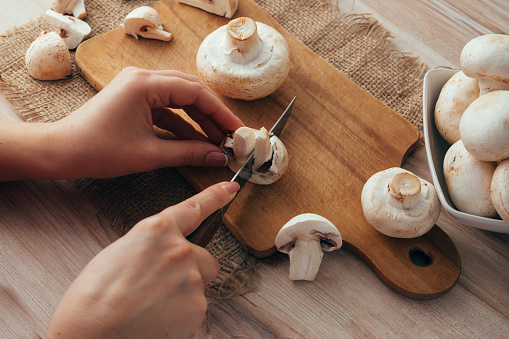 Mushrooms on a cutting board. Champignon mushrooms on a wood cutting board. Woman cook slicing food. Top down view.